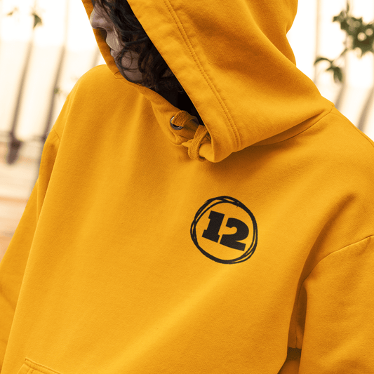 Model wearing yellow hoodie featuring minimal black “12” circle emblem on chest, clean unisex streetwear by LostLogicCo Canada