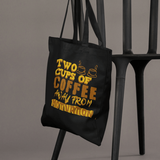 Eco tote bag with “Two Cups of Coffee Away from Motivation” typography design in brown and yellow on black organic cotton by LostLogicCo Canada.