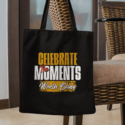 Eco tote bag with “Celebrate the Moments Worth Living” typography design in white, gold, and yellow on black organic cotton by LostLogicCo Canada.