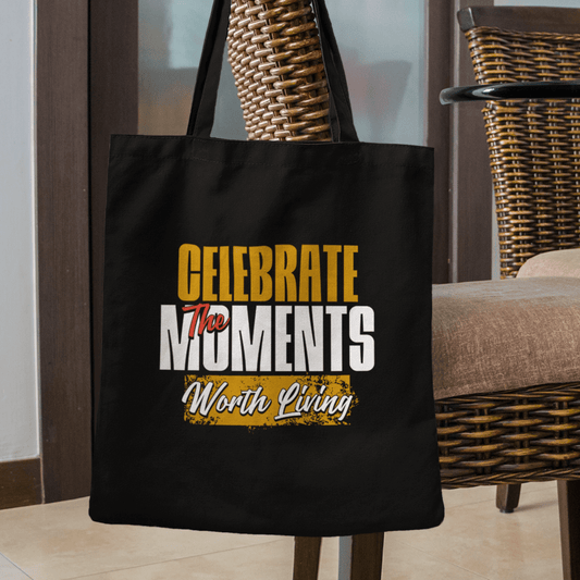 Eco tote bag with “Celebrate the Moments Worth Living” typography design in white, gold, and yellow on black organic cotton by LostLogicCo Canada.