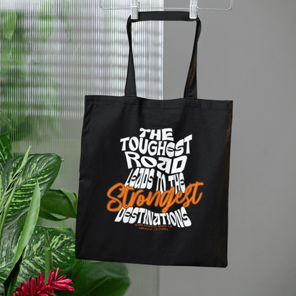 Eco tote bag with “The Toughest Road Leads to the Strongest Destinations” motivational typography design in white and orange on black organic cotton by LostLogicCo Canada.